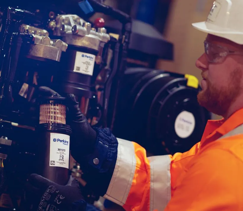 Perkins worker in a high visibility jacket working on an engine.